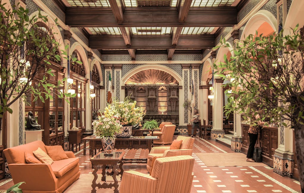 A luxurious hotel lobby featuring elegant architecture, rich decor, and comfortable seating under a stained glass ceiling.