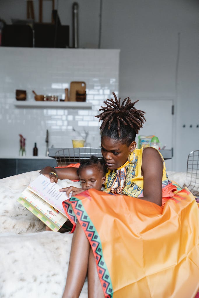 A nurturing moment as a mother and child read a book together on a cozy couch indoors.