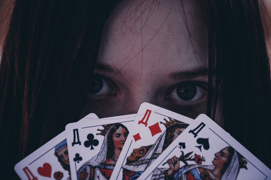 Close-up of a girl's eyes peering over a spread of playing cards, evoking mystery and intrigue.