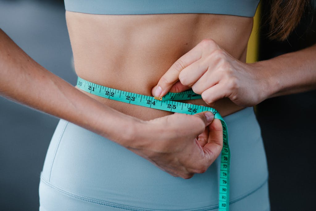 Close-up of a woman measuring her waist with a tape, representing fitness, health, and weight loss.