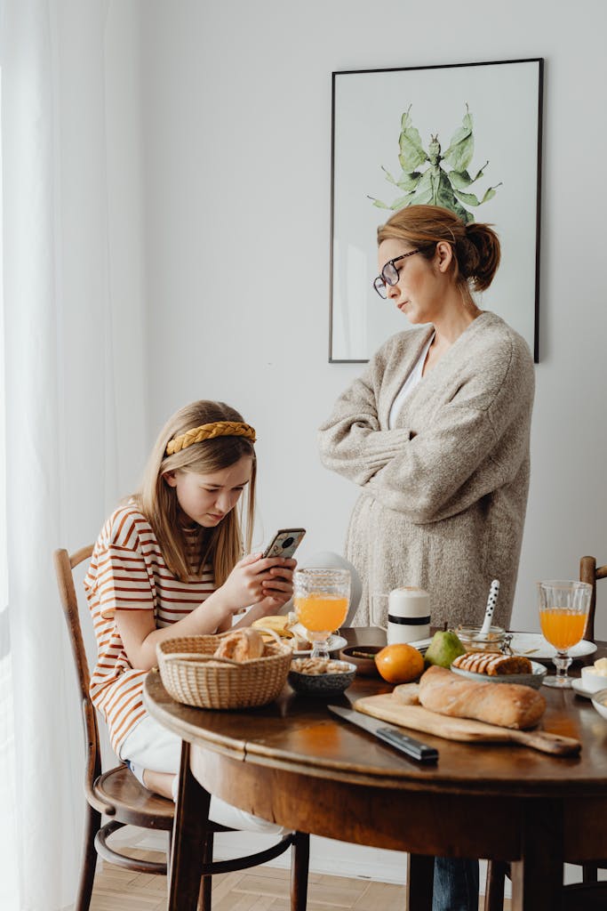 Mother upset with daughter using smartphone at breakfast table with food.