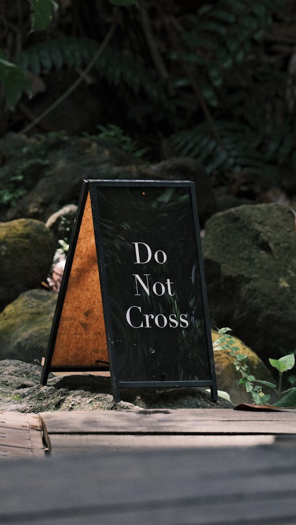 Sign reading 'Do Not Cross' amidst rocks and foliage in a natural setting.