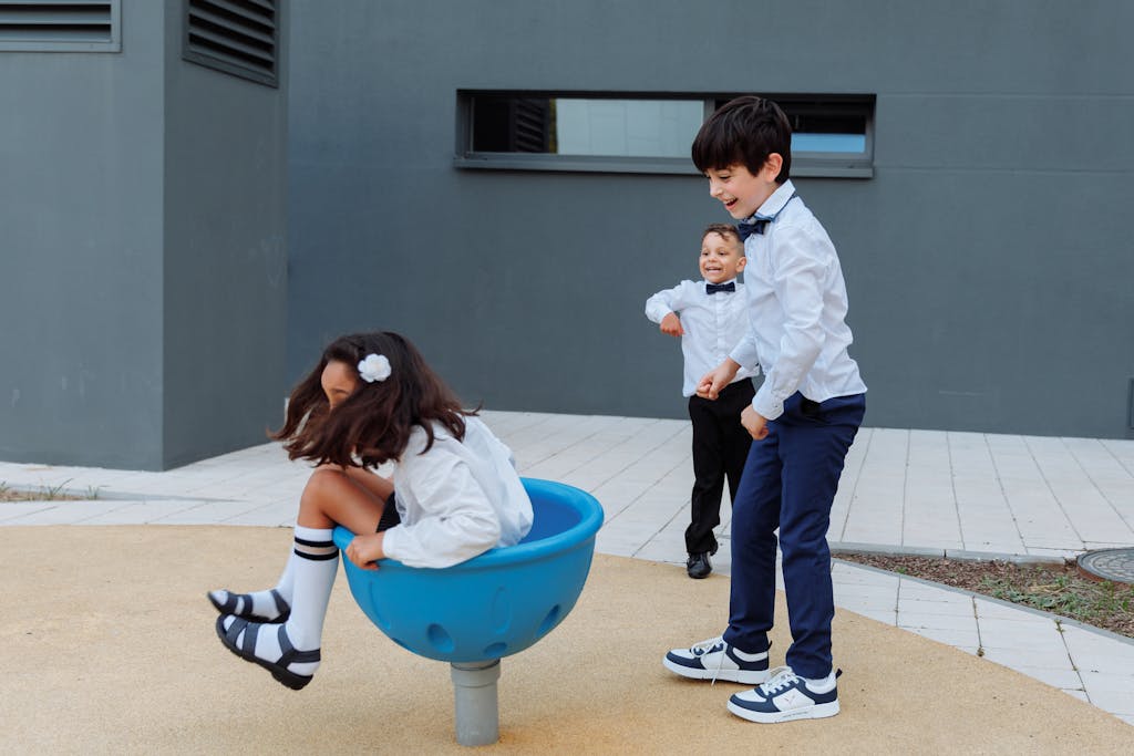 Three children in formal attire enjoy playful moments at a modern outdoor playground.