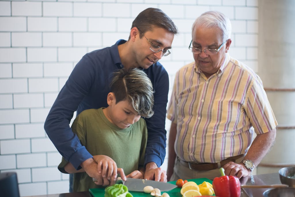 Three generations cooking together, sharing skills and family moments in a bright kitchen.